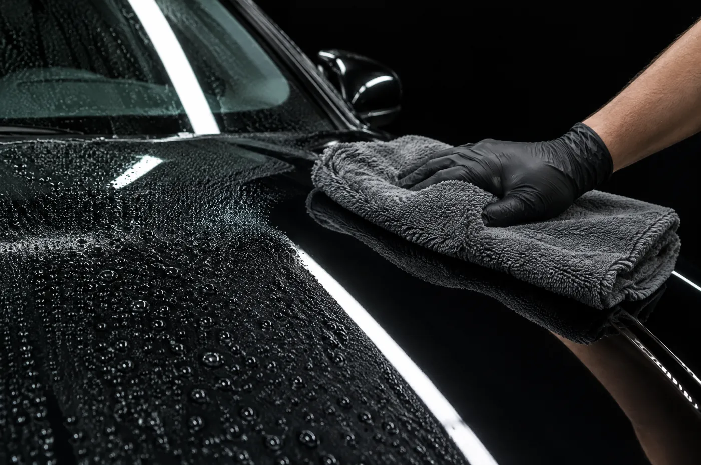 A gloved hand drying a black bonnet with a microfibre towel